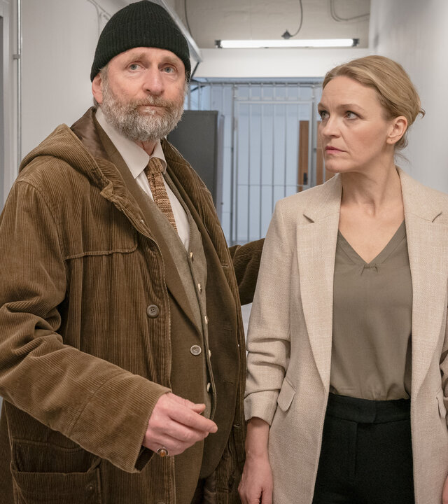 "SOKO Leipzig - Angeklagt": Jan (Marco Girnth), Leni (Caroline Scholze) und Dr. Egon Fleischbauer (Jörg Witte) stehen in einem grauen Flur. Im Hintergrund sind Gitterstäbe zu sehen. Fleischbauer steht neben Leni, die ihn anschaut. Er drückt seine Hand gegen Lenis Rücken und schaut nach vorne. Hinter Leni steht Jan und schaut Fleischbauer an.