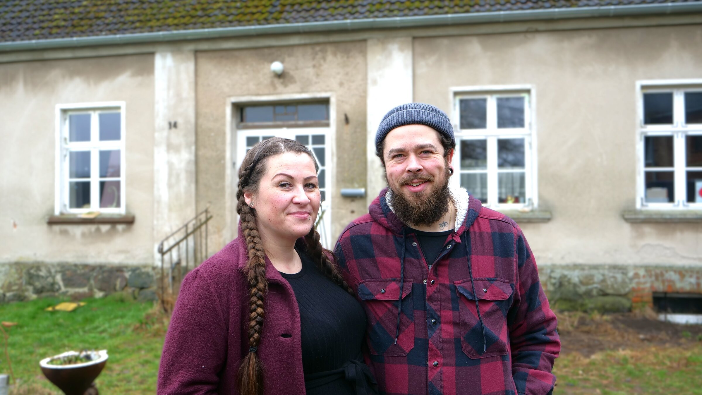 "ZDF.reportage: Großprojekt Hausbau": Sara und Max stehen nebeneinander vor einem alten Haus und blicken lächelnd in die Kamera.