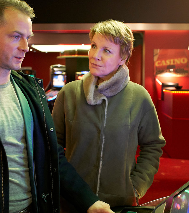 "Marie Brand und das Spiel mit dem Glück": Die beiden Kommissare stehen vor einem Spielautomaten im Spielcasino. Jürgen Simmel bedient den Automaten und Marie Brand schaut ihn verwundert an.