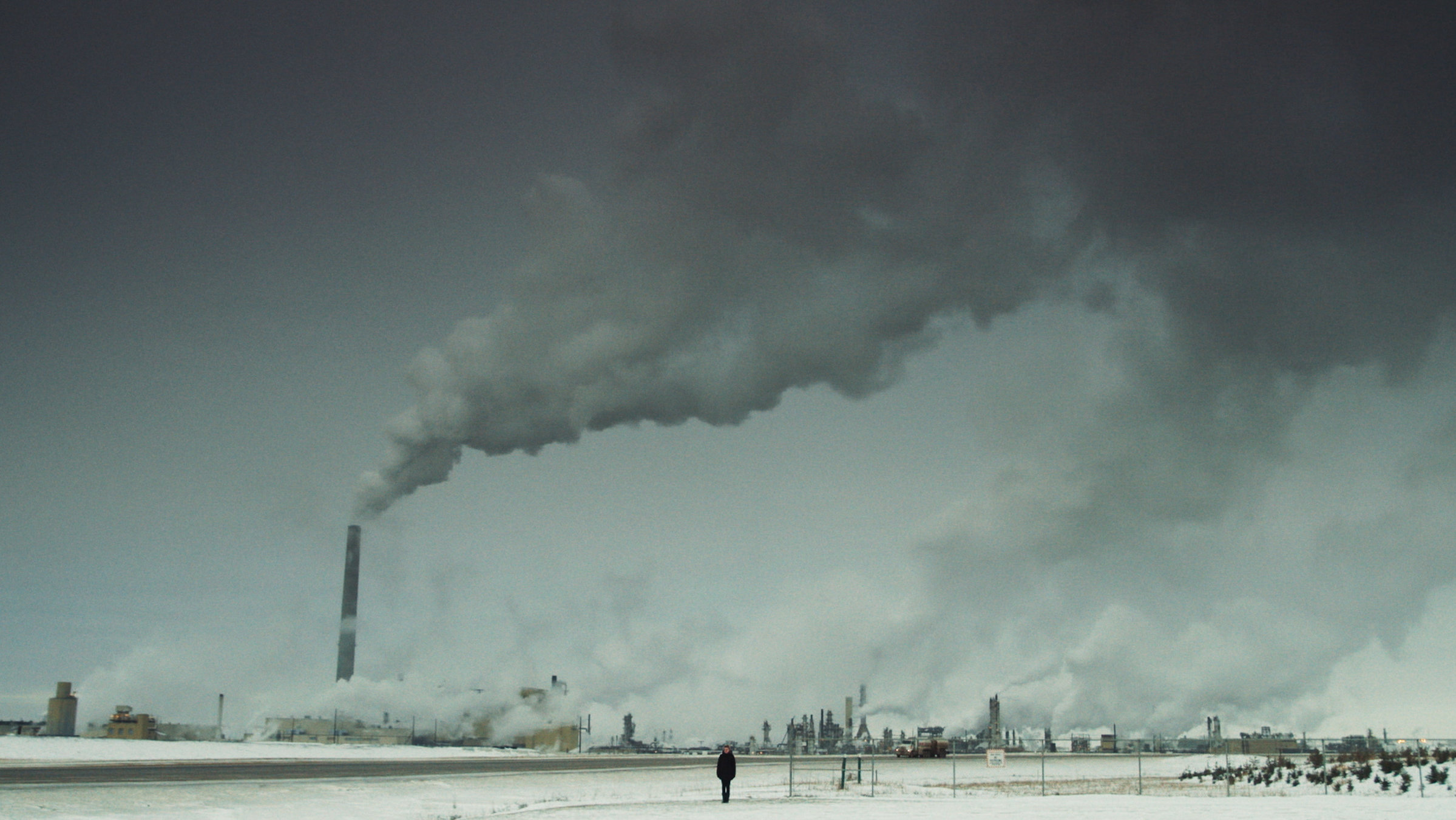 "Dark Eden": Riesige Industrieanlage mit Schloten, in der Mitte des Bildes ganz kleine eine junge Frau.