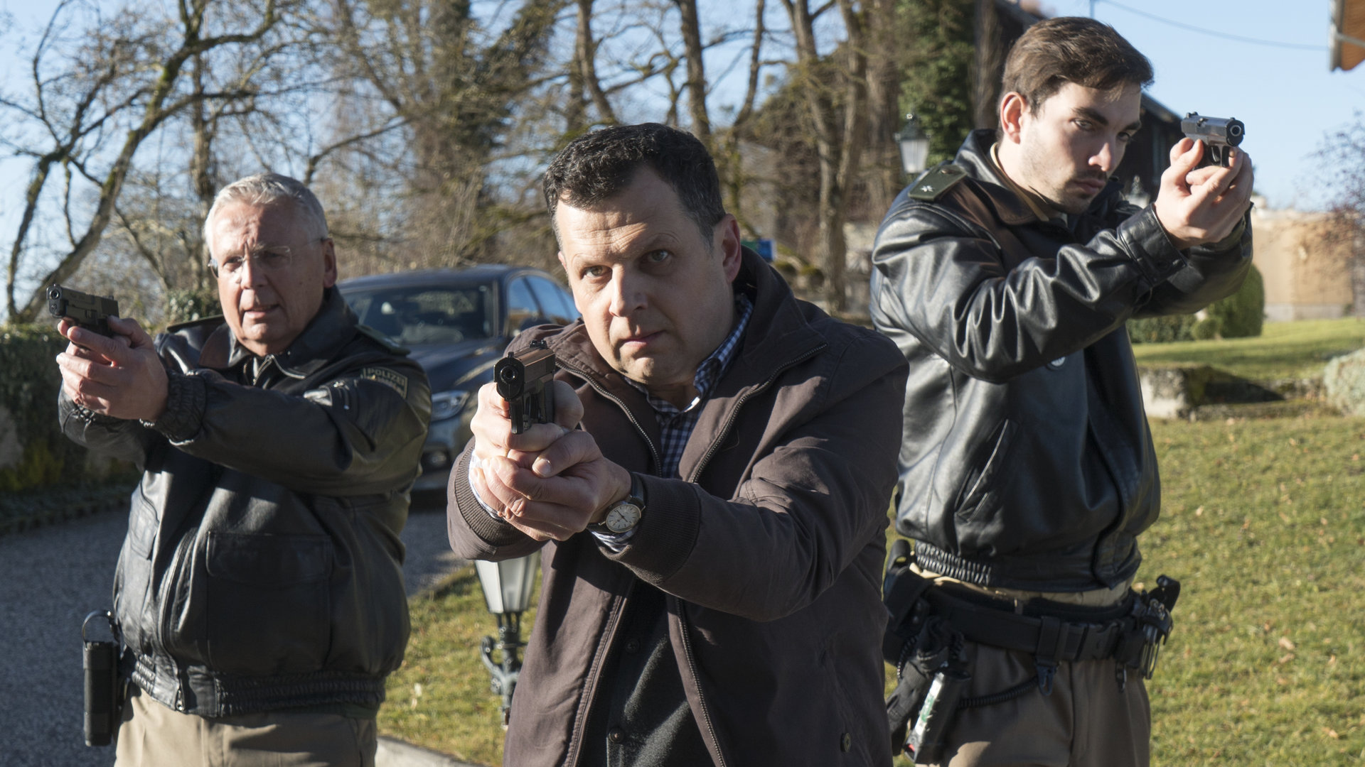 „Laim und die Zeichen des Todes“: Anton Simhandl (Gerhard Wittmann) und seine Kollegen stehen mit vorgehaltenen Waffen auf einem Weg.