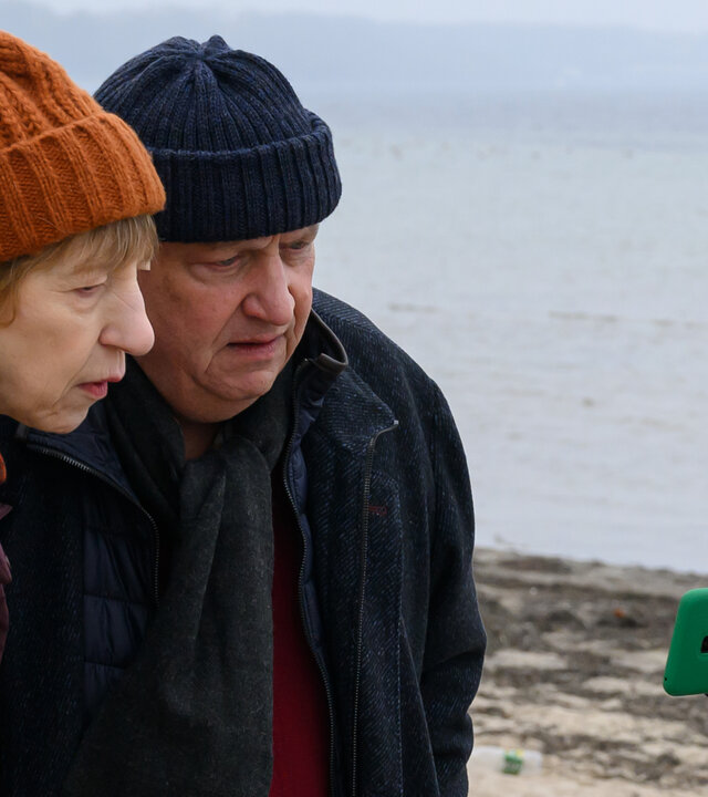 "SOKO Wismar – Schöne Küste": Rechtsmedizinerin Dr. Helene Sturbeck (Katharina Blaschke) und Revierchef Jan-Hinrich Reuter (Udo Kroschwald) betrachten am Strand das Foto der vermissten Nele Köster.