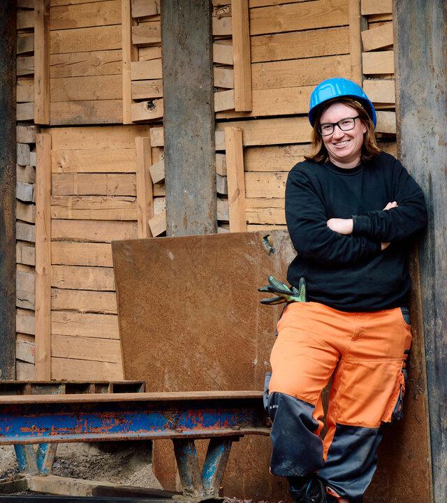 "einfach Mensch - Delia Buchhorn: Grenzt mich nicht aus": Delia Buchhorn steht in Schutzkleidung mit Helm auf einer Baustelle vor einer Holzwand und schaut lächelnd in die Kamera.