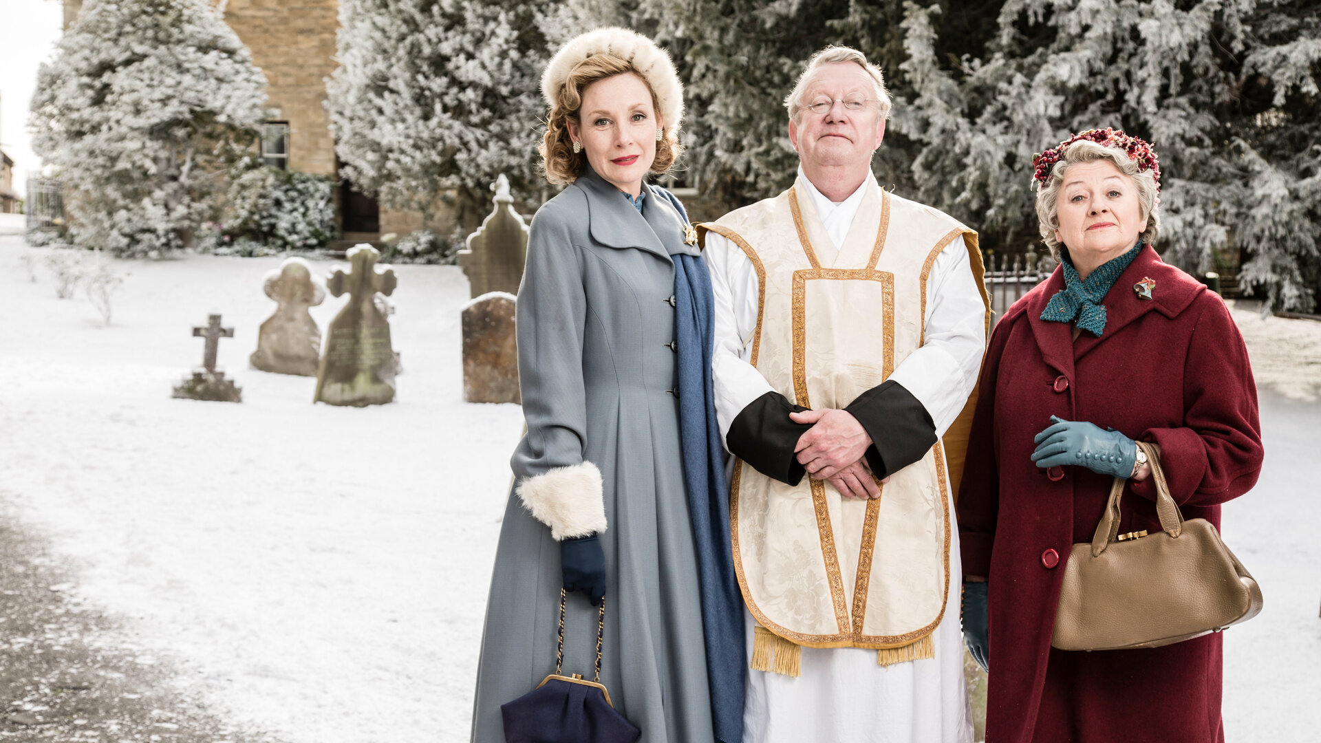"Father Brown - Ein Frohes Fest": Lady Felicia (Nancy Carroll), Father Brown (Mark Williams) und Mrs. McCarthy (Sorcha Cusack) stehen nebeneinander vor einem verschneiten Friedhof.