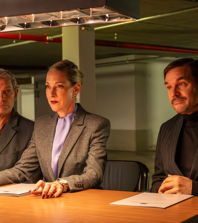"SPYON - Der perfekte Spion": Ausbilder Voss (Götz Otto), Ausbilderin Haberland (Sophie von Kessel) und Ausbilder Kocabay (Alexander Beyer) sitzen nebeneinander an einem Tisch und schauen in die Ferne. Vor den dreien liegen Bewerbungsmappen.