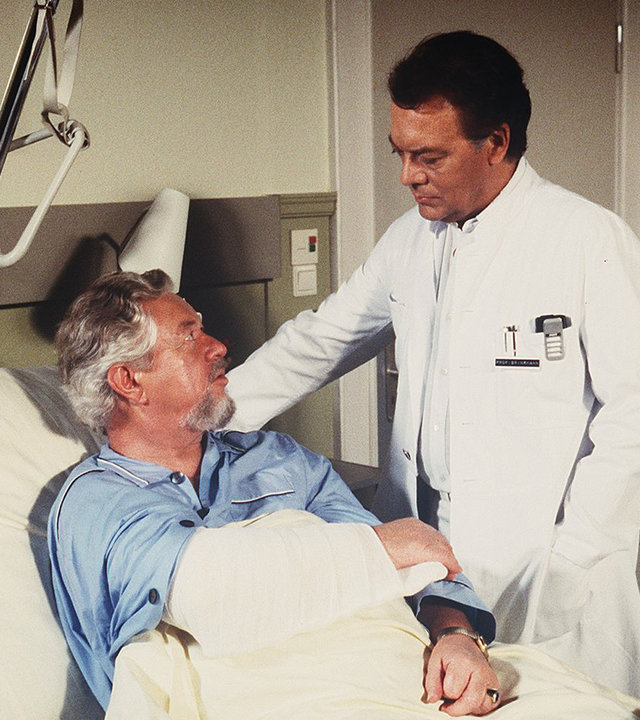 "Die Schwarzwaldklinik - Besuch aus Kanada": Willi Anschütz (Klaus Havenstein) liegt im Krankenbett. Neben ihm am Bett steht Prof. Brinkmann (Klausjürgen Wussow).