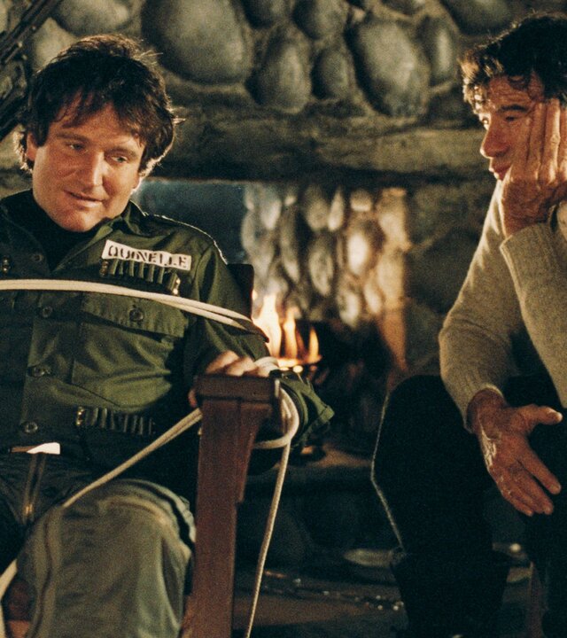 "Die Überlebenskünstler": Donald Quinelle (Robin Williams) sitzt gefesselt auf einem Stuhl. Sonny Paluso (Walter Matthau) sitzt daneben und betrachtet ihn ruhig. Er stützt sein Kinn auf einer Hand ab.