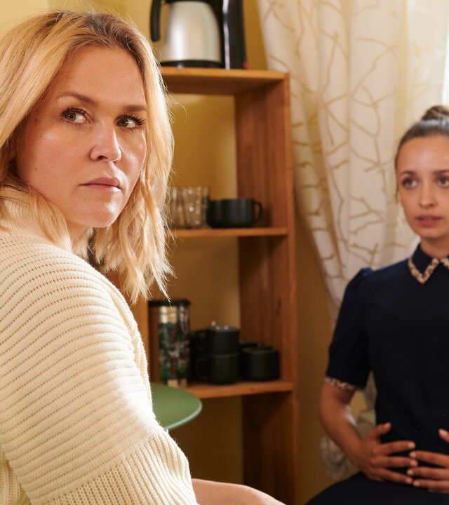 "Lena Lorenz - Lügenbaby": Lena Lorenz (Judith Hoersch) sitzt Flora Bergmann (Nellie Thalbach) in einem Aufenthaltsraum gegenüber. Flora hält sich ihren schwangeren Bauch, Lena hat sich nach vorne gedreht und blickt ernst.