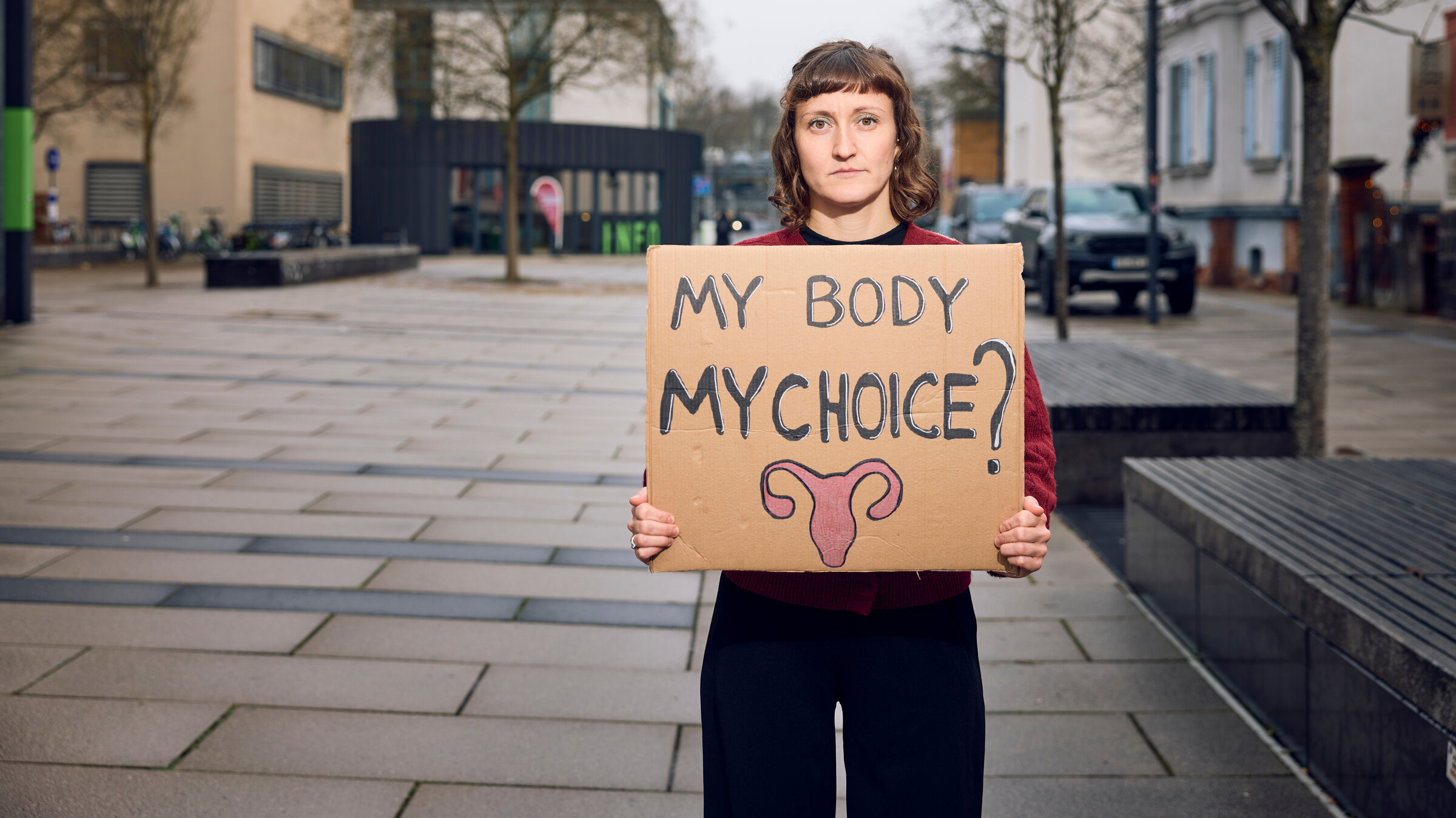 "Ungeplant schwanger": Klara sthet auf einem Platz in der Stadt und hält ein Schild in der Hand mit der Aufschrift "My Body My Choice?".