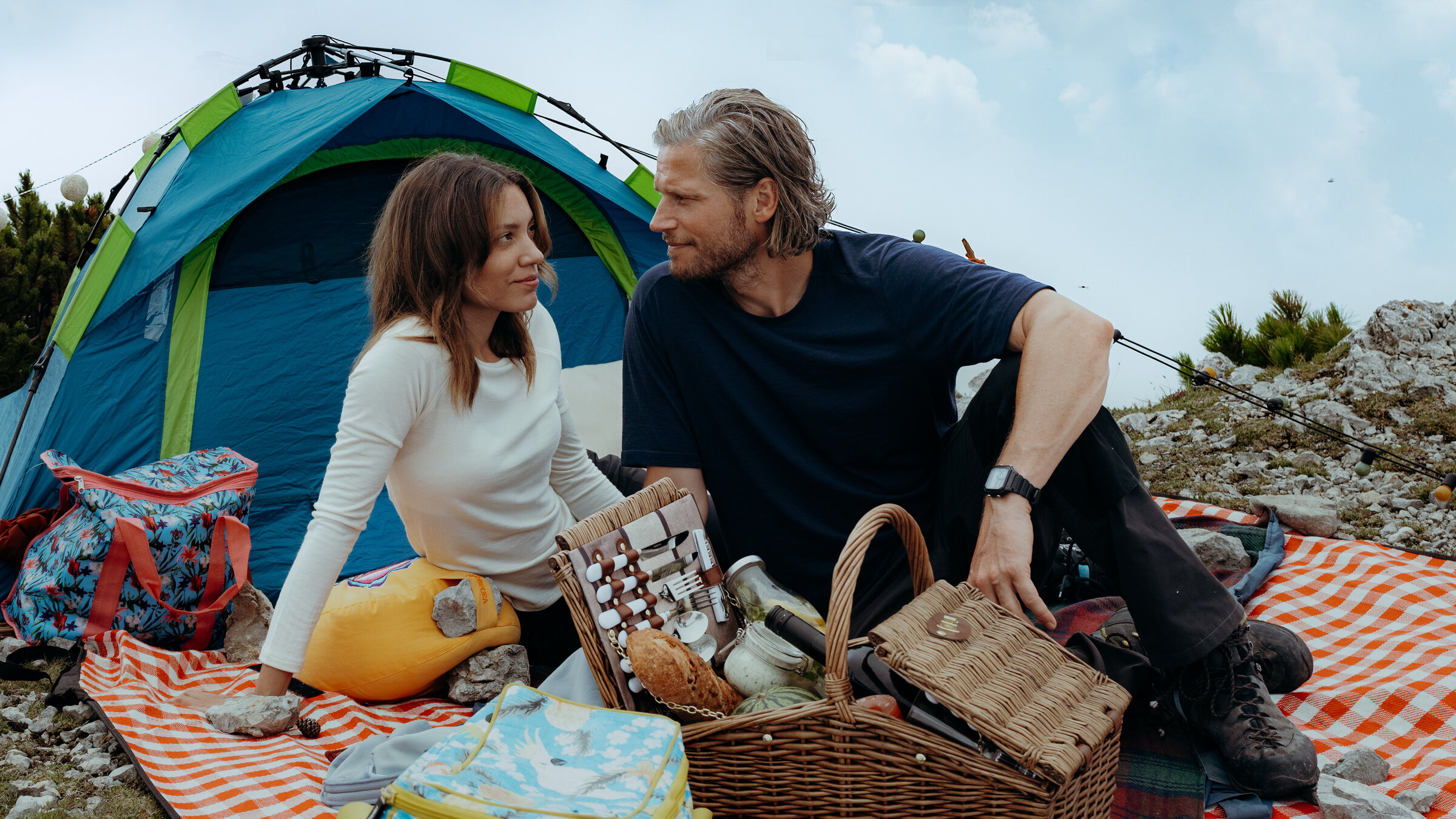 "Die Bergretter: Ein letzter Augenblick": Auf einem Berggipfel: Auf einer Picknickdecke sitzen Alex (Viktoria Ngotsé) und Markus (Sebastian Ströbel) und blicken sich tief in die Augen. Vor ihnen steht ein gefüllter Picknickkorb, hinter ihnen ist ein Zelt aufgebaut.