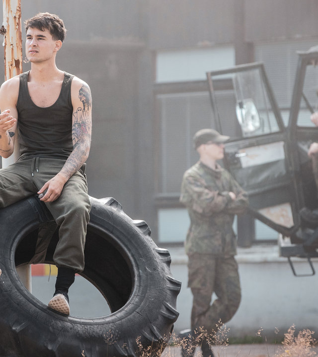 "Californian Commando - Der Schutzengel": Van (Kian Lawley) sitzt auf einem Reifen und schaut nachdenklich zur Seite.