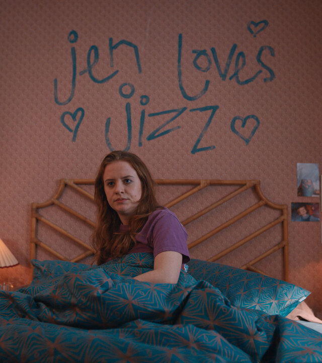 "Extraordinary - Überraschung": Jen (Máiréad Tyers) liegt in ihrem Bett und mustert ihr Schlafzimmer mit skeptischem Blick. Auf der Tapete hinter ihr steht in blauer Farbe an die Wand geschrieben "jen loves jizz".