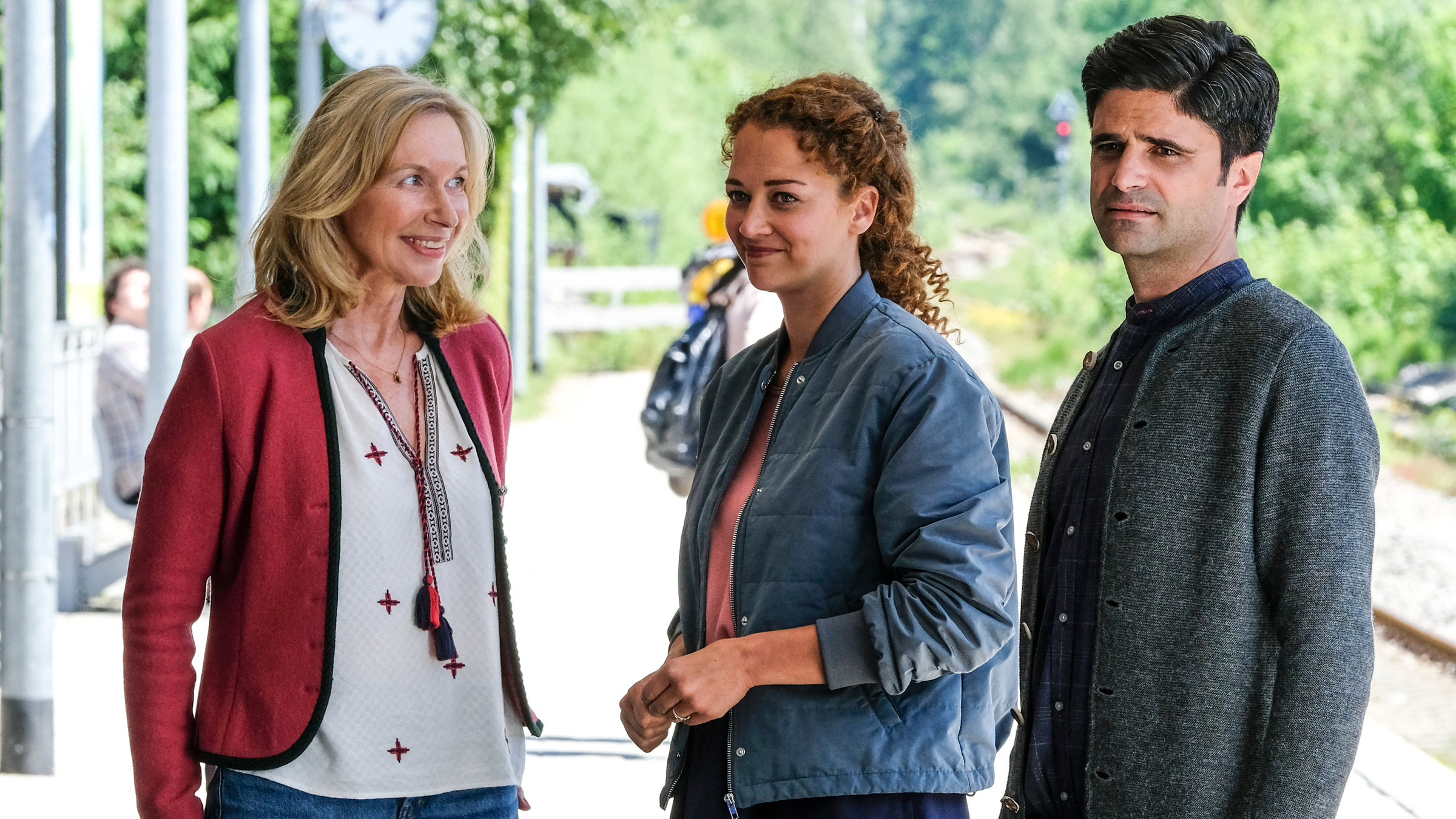 "Tonio & Julia - Nesthocker": Auf einem Bahnsteig stehen Tanja Clemens (Therese Hämer), Julia Schindel (Oona Devi Liebich) und Tonio Niederegger (Maximilian Grill) beieinander. Alle drei lächeln.