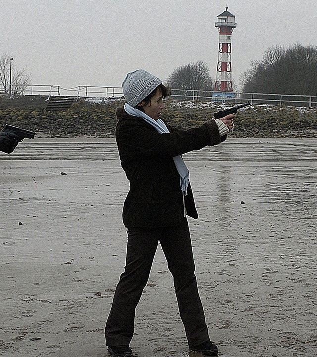 "Notruf Hafenkante - Das kalte Herz": Auf dem Wattenmeer bedroht Bettina Schmidt (Anke Sevenich) Nils (Thomas Scharff) mit einer Pistole. Melanie (Sanna Englund) steht daneben und bedroht wiederum Bettina Schmidt mit ihrer Waffe.