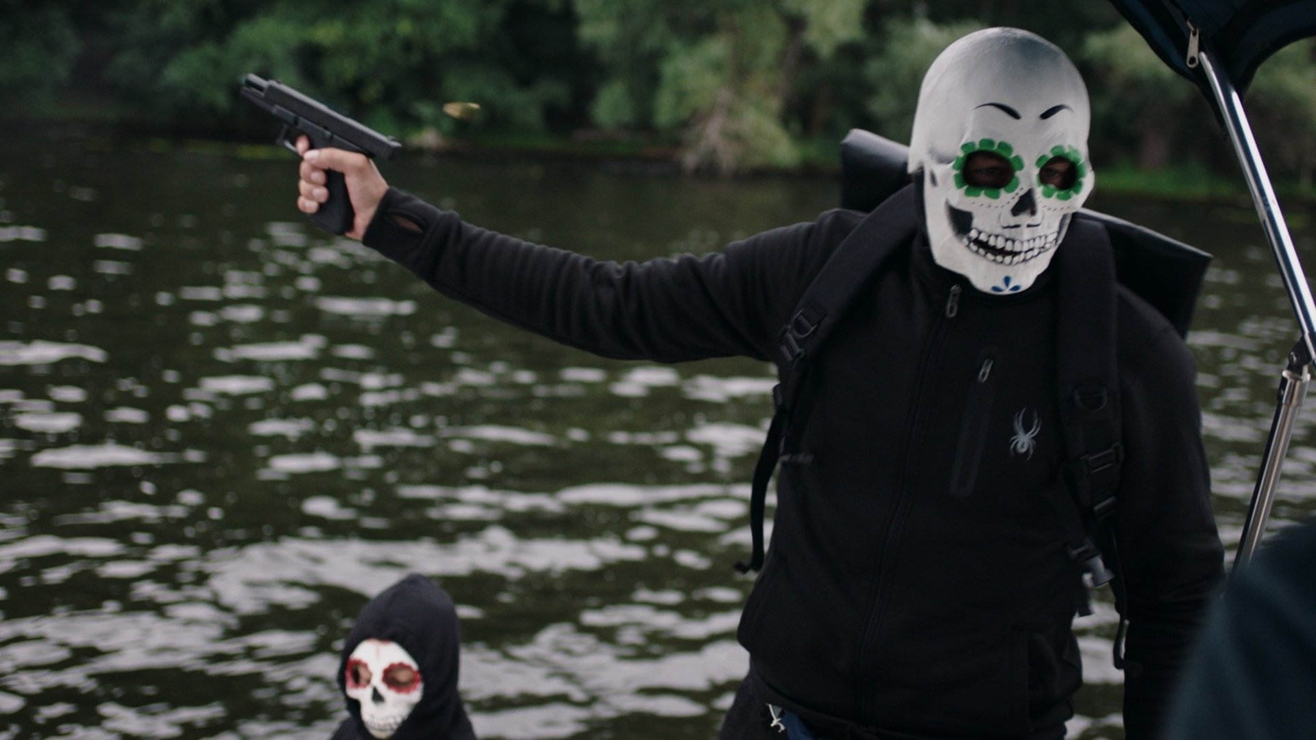 "SOKO Potsdam - Smoke on the water": Auf der Havel in einem Motorboot befinden sich zwei maskierte Personen. Die eine maskierte Person richtet eine Pistole nach links und schaut zu einer weiteren Person, die nicht im Bild ist.