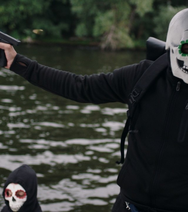 "SOKO Potsdam - Smoke on the water": Auf der Havel in einem Motorboot befinden sich zwei maskierte Personen. Die eine maskierte Person richtet eine Pistole nach links und schaut zu einer weiteren Person, die nicht im Bild ist.
