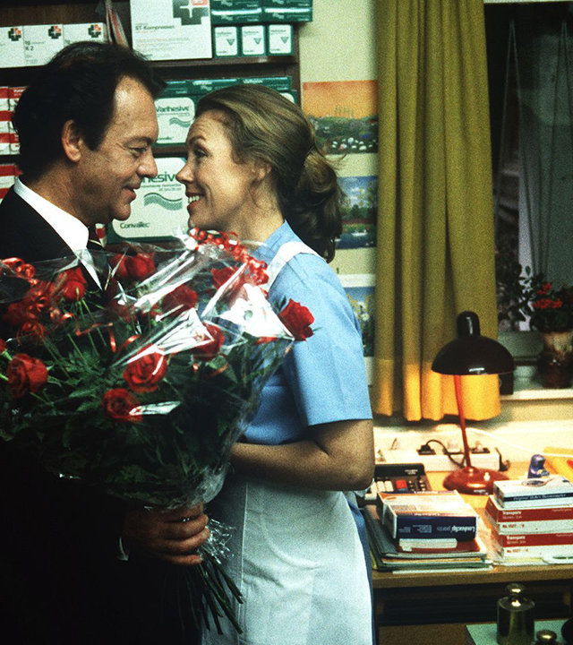 "Die Schwarzwaldklinik - Die Mutprobe": Prof. Brinkmann (Klausjürgen Wussow) besucht Christa (Gaby Dohm) an ihrem Arbeitsplatz und überrascht sie mit einem großen Blumenstrauß.