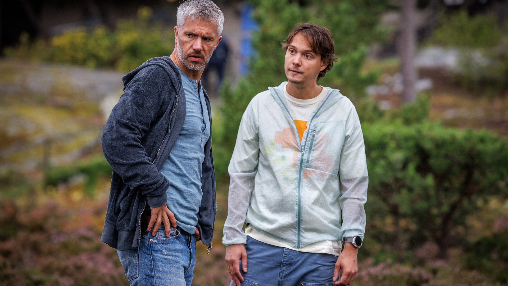 "Mord im Mittsommer - Nikki & Evelina": Alexander (Nicolai Cleve Broch) und Welpe (Julius Fleischanderl) stehen im Freien nebeneinander. Alexander wirkt skeptisch. Welpe blickt in seine Richtung.