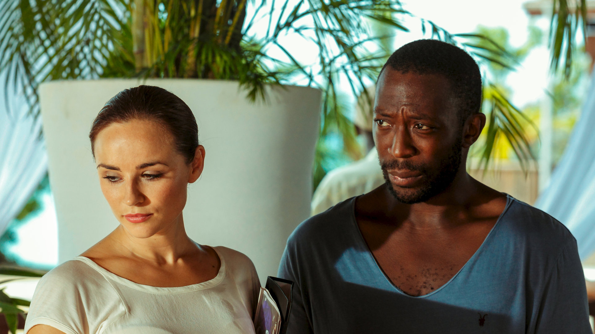 "Death in Paradise: Der 3-Uhr-Tee": Anna Jones (Emma Pierson) und Paul Vincent (Shaun Parkes) stehen nebeneinander. Anna Jones schaut traurig nach unten, und Paul Vincent sieht besorgt zur Seite.