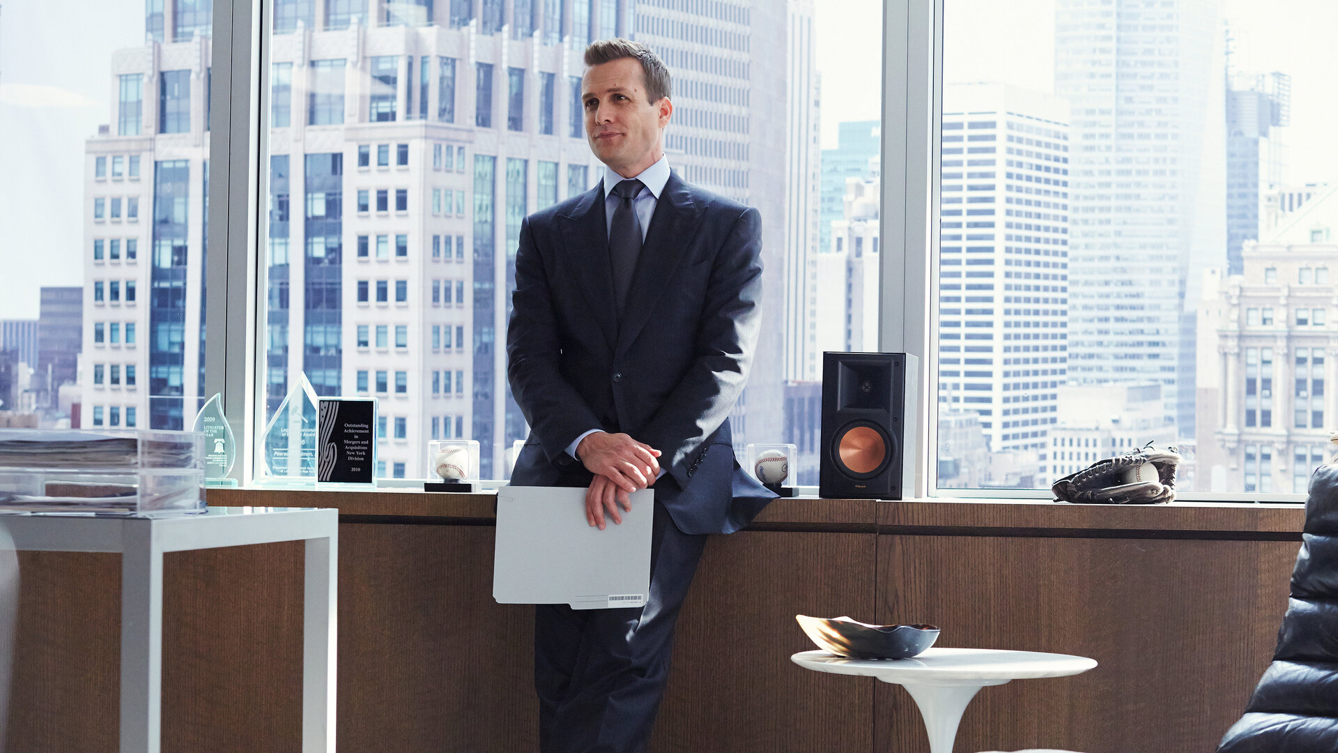"Suits - Private Einsichten": Harvey (Gabriel Macht) steht im Anzug in einem Büro, lässig an ein Sideboard gelehnt. Hinter ihm sind große Fenster mit Blick auf die Skyline zu sehen.