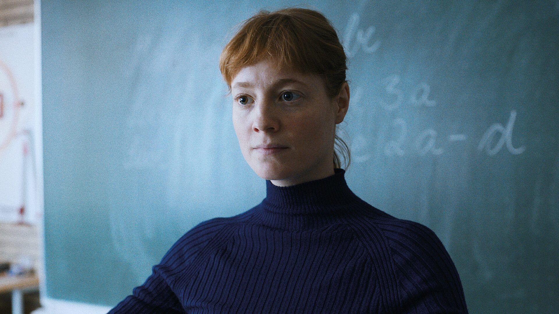 "Das Lehrerzimmer": Carla Nowak (Leonie Benesch) steht mit ausgebreiteten Armen vor einer großen Schultafel und schaut mit fragendem Blick vor sich ins Klassenzimmer.
