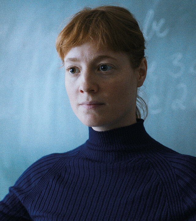 "Das Lehrerzimmer": Carla Nowak (Leonie Benesch) steht mit ausgebreiteten Armen vor einer großen Schultafel und schaut mit fragendem Blick vor sich ins Klassenzimmer.