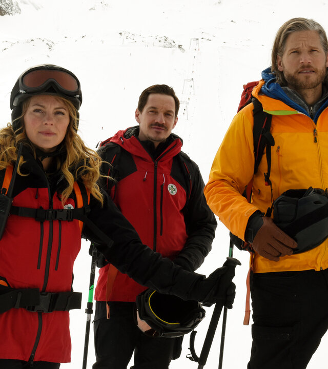 "Die Bergretter - Späte Reue (2)": In einer Schneelandschaft: Die Bergretter Markus (Sebastian Ströbel), Katharina (Luise Bähr) und Tobi (Markus Brandl) stehen auf Skiern vor einer Pistenkarte.