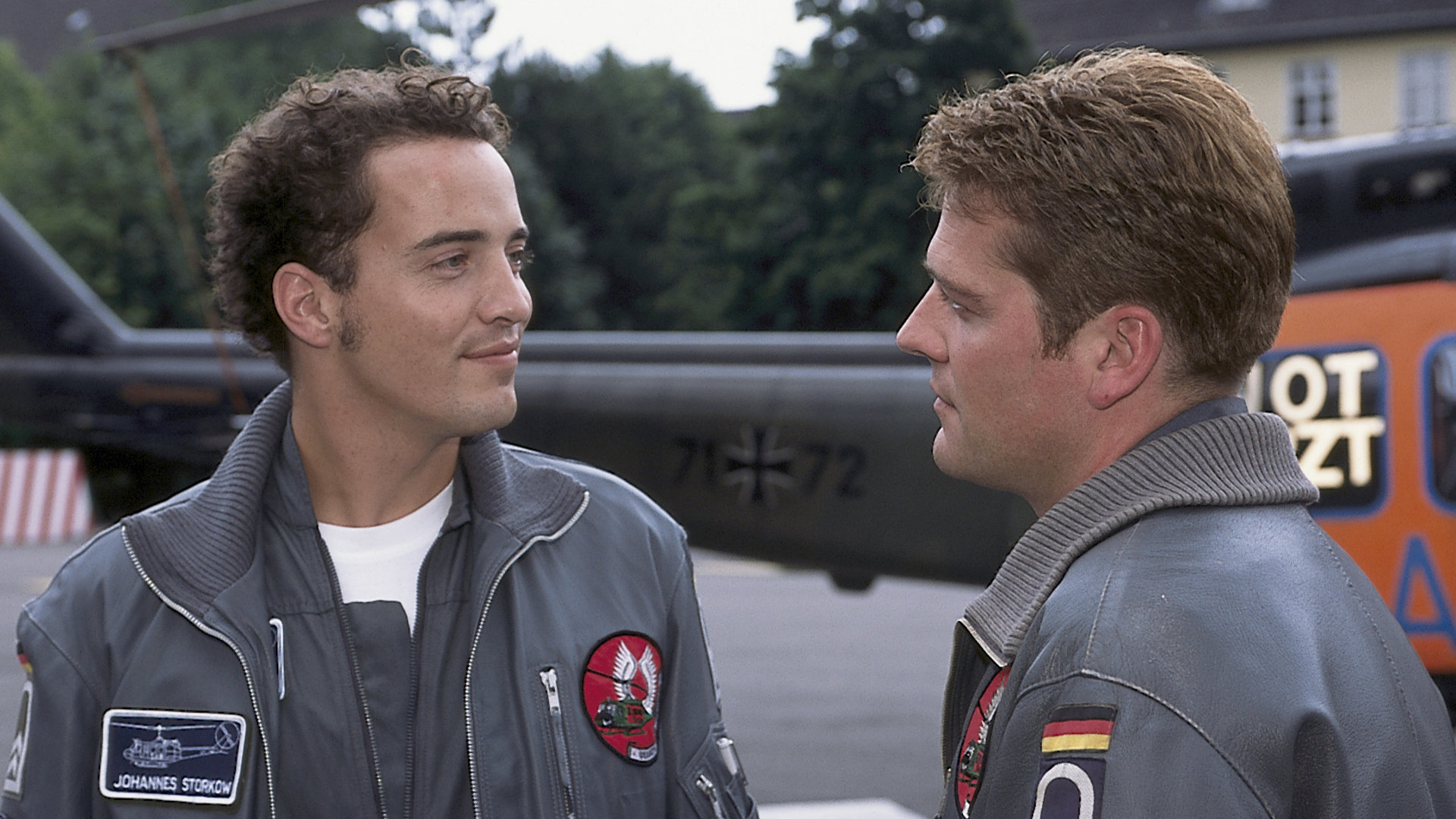 "Die Rettungsflieger - Der Ersatzmann": Wollcke (Oliver Hörner) und Johannes von Storkow (Patrick Wolff) stehen neben dem Hubschrauber und unterhalten sich.