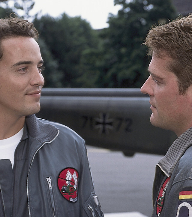 "Die Rettungsflieger - Der Ersatzmann": Wollcke (Oliver Hörner) und Johannes von Storkow (Patrick Wolff) stehen neben dem Hubschrauber und unterhalten sich.