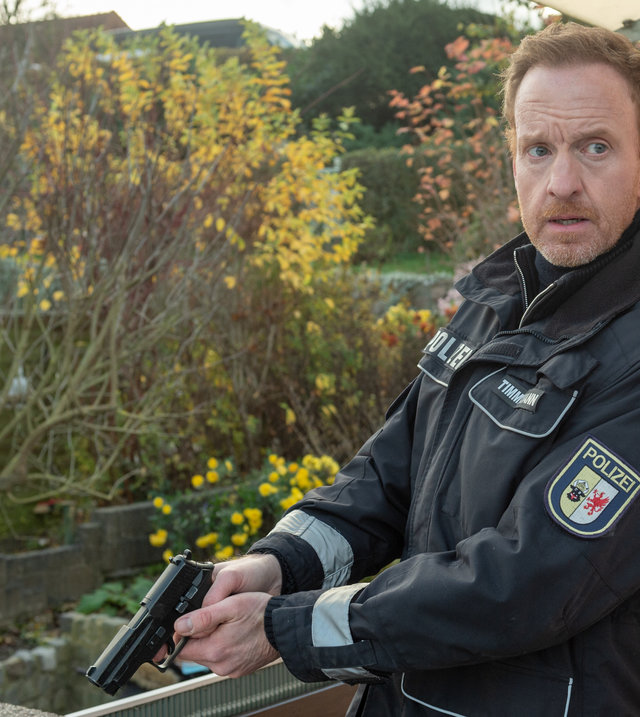 "SOKO Wismar – Schmerz": In einer Kleingartenkolonie steht Polizeihauptmeister Kai Timmermann (Mathias Junge) mit konzentriertem Blick hinter einer Hausecke in Deckung. Er hat die Dienstpistole schussbereit in beiden Händen und ist kurz davor, die Gartenlaube zu stürmen, in der er den Verdächtigten vermutet.