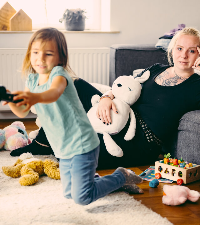 "37°Leben: Ich will keine Kinder": Linda sitzt im Wohnzimmer vor dem Sofa, neben ihr spielen zwei Kinder.