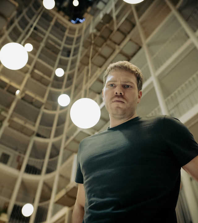 "Another Monday - Der Wiedergänger": Moritz Becker (Ben Münchow) steht vor der Kamera und blickt in die Ferne. Im Hintergrund ist eine Hochhausfassade zu sehen.