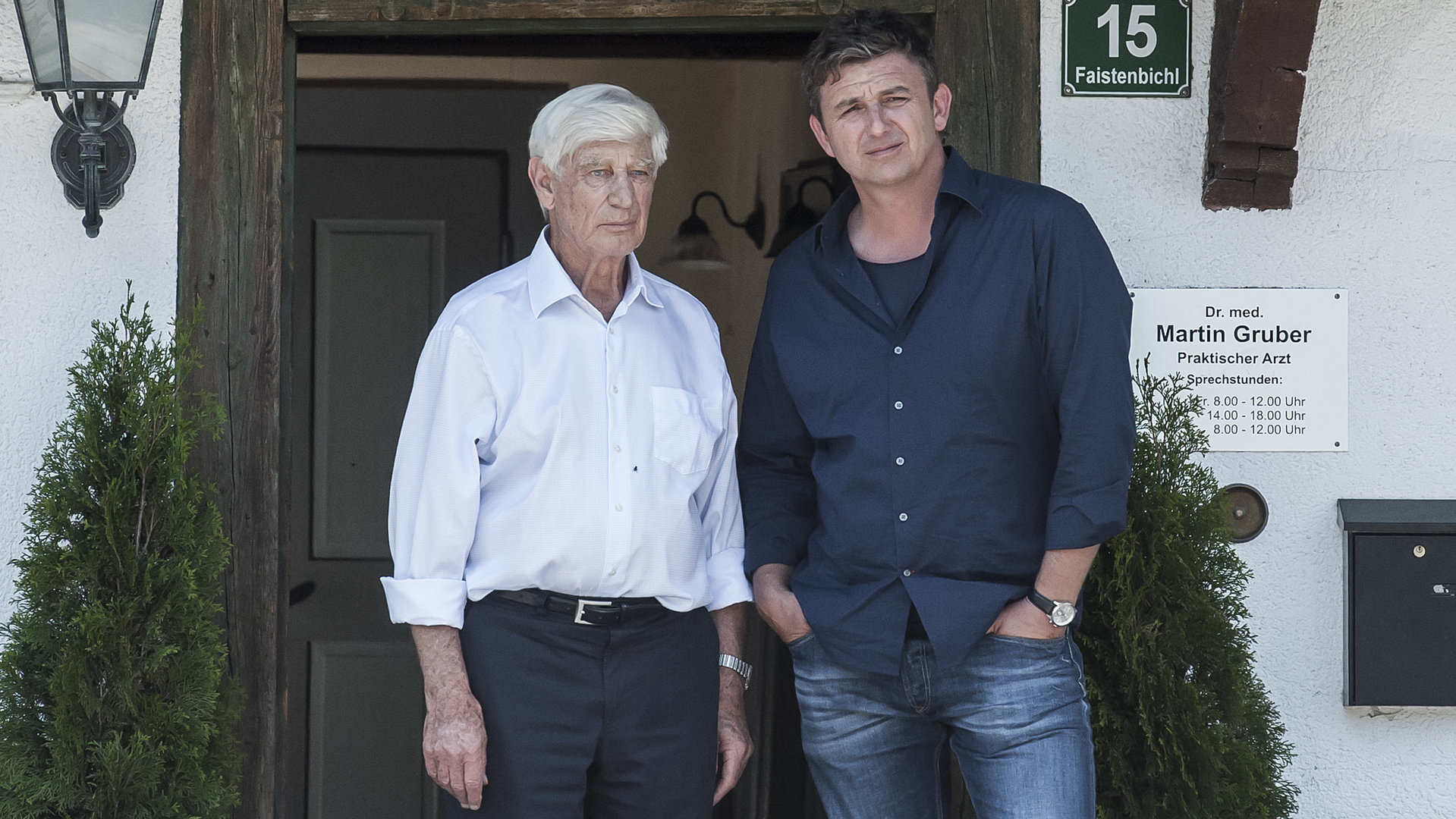 "Der Bergdoktor - Alte Wunden (1)": Dr. Roman Melchinger (Siegfried Rauch) und Dr. Martin Gruber (Hans Sigl) stehen vor der Praxis. Beide schauen grübelnd in die Kamera.
