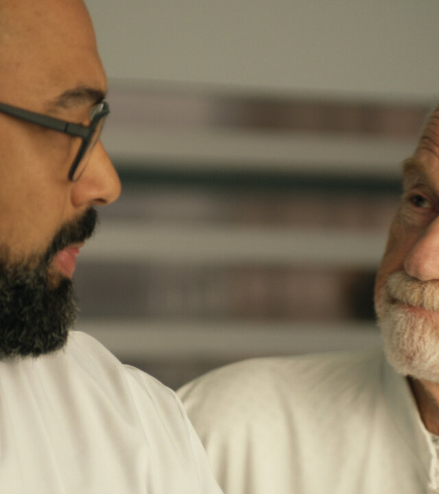 "Notruf Hafenkante - Erlösung": Großaufnahme: Dr. Evans (Tino Führer) und Ulrich Isensee (Dietrich Hollinderbäumer) stehen dicht nebeneinander und schauen sich an. Beide tragen weiße Arztkittel.