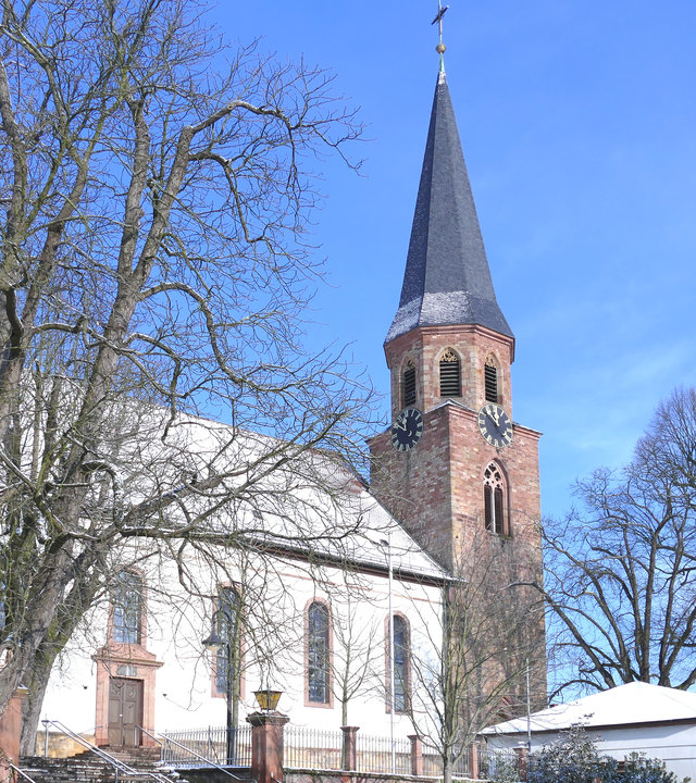 "Katholischer Gottesdienst - Die Liebe weitertragen": Außenansicht der Kirche Mariä Himmelfahrt in Herxheim im Winter, es liegt bei Schnee.