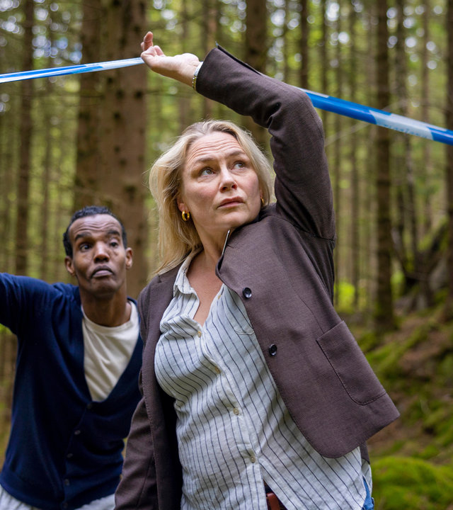 "Detective No. 24: Hase und Igel": Ibraahin (Nasir Farah Dhagole) und Tilda (Malin Levanon) sind im Wald. Tilda hebt das Absperrband der Polizei an und geht darunter durch. Ibraahin folgt ihr.