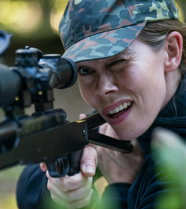 "Oxen - Staats-Affären": Kajsa (Birgitte Hjort Sørensen) hat ein Gewehr mit Zielfernrohr im Anschlag. Sie befindet sich im Wald und trägt eine Camouflage-Kappe.