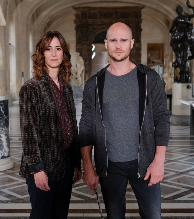 "Art of Crime - Der Da Vinci Code (1)": Florence Chassagne (Éléonore Gosset) und Antoine Verlay (Nicolas Gob) stehen in einem großen Museumsraum mit antiken Statuen und Schaukästen und schauen in die Kamera.