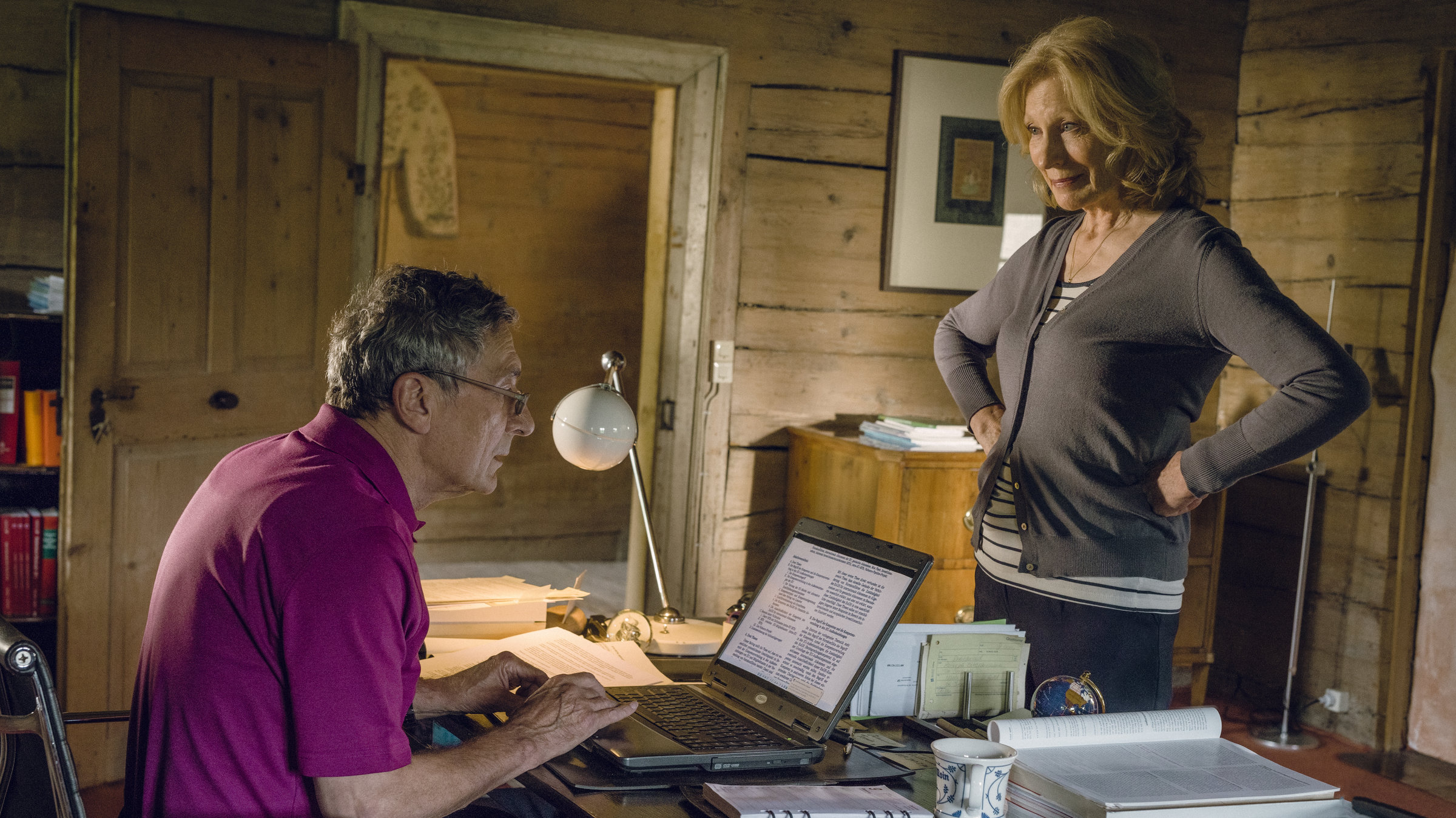 "Jella jagt das Glück": Klaus (Rudolf Kowalski) sitzt mit Laptop am Schreibtisch, Jella (Maren Kroymann) steht ihm gegenüber, ihre Arme seitlich an der Taille.