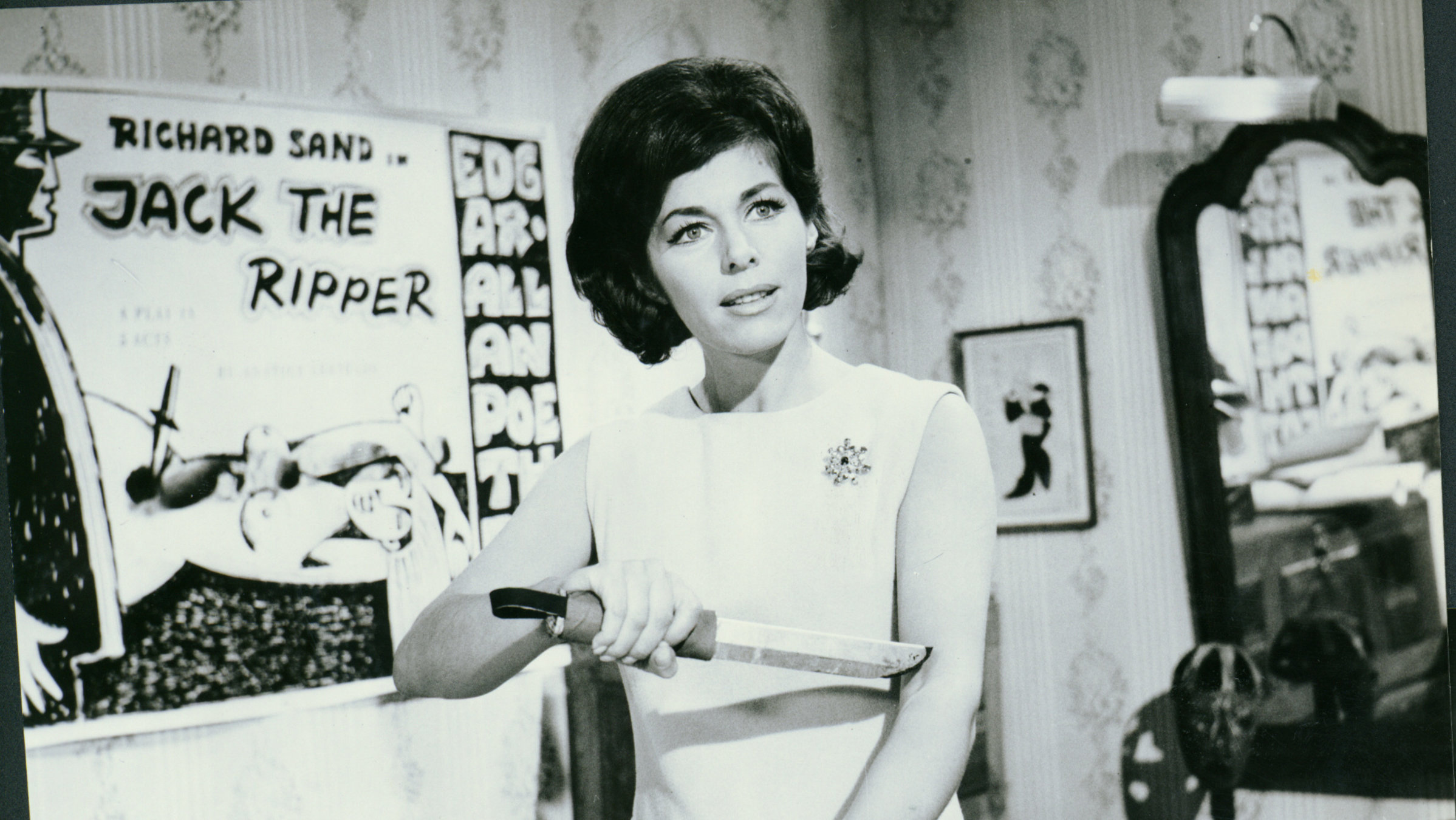 “Das Ungeheuer von London-City“: Ann Morlay (Marianne Koch) hält sich ein Messer mit langer Klinge in die Ellenbeuge ihres ausgestreckten Armes und hat dabei einen verwunderten Gesichtsausdruck.