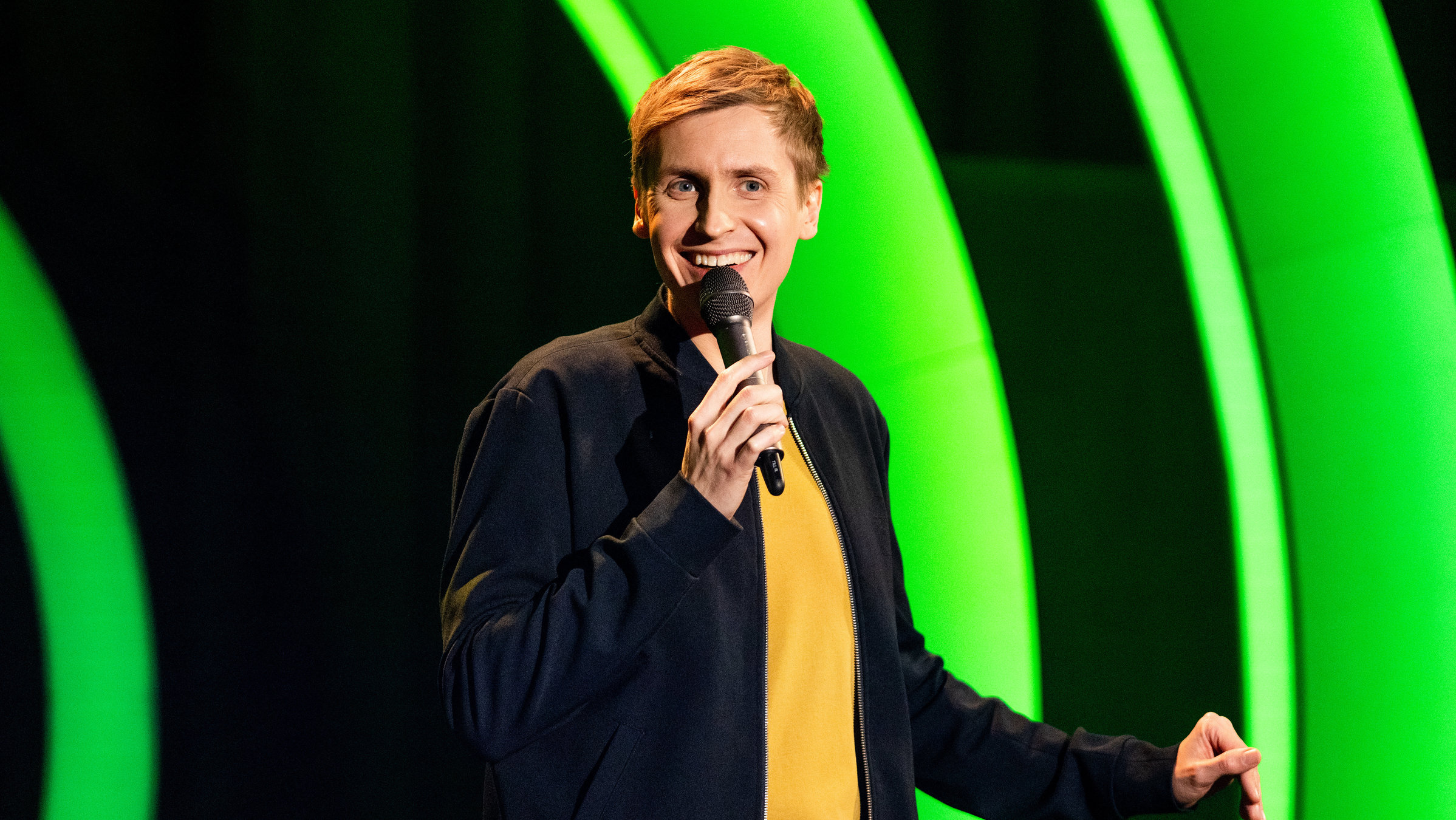 "Till Reiners: Bescheidenheit XS": Till Reiners steht auf der Bühne im Frankfurter Hof in Mainz und präsentiert sein Programm. Dabei lacht er in die Kamera.