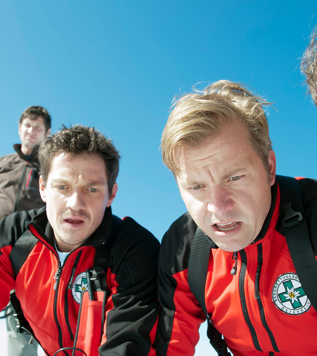 "Die Bergretter: Tödliches Vertrauen - Teil 1": Die Bergretter Tobias (Markus Brandl), Toni (Martin Klempnow) und Michael (Robert Lohr) schauen mit entsetzten Gesichtern in eine Felsspalte hinab. Hinter ihnen steht Hans Baumann (Andreas Kiendl) und beobachtet die Szene.