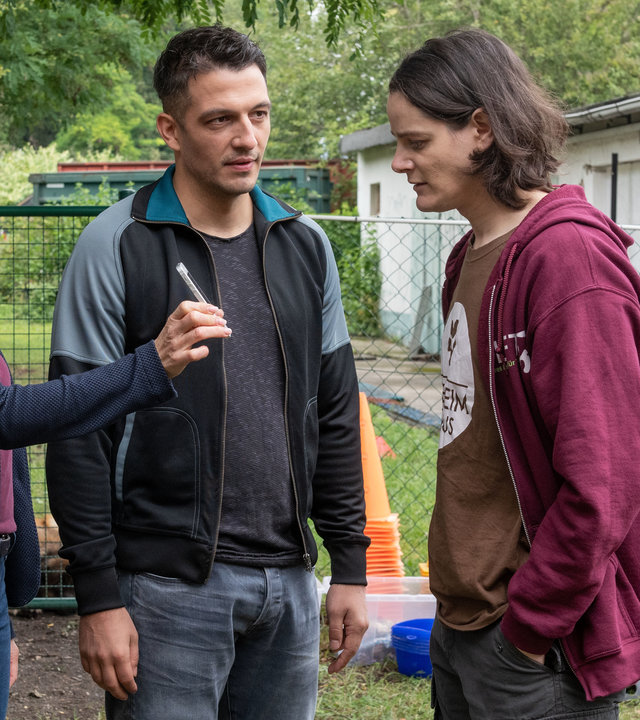 "Der Staatsanwalt - Fangschuss": Kerstin Klar (Fiona Coors), Max Fischer (Max Hemmersdorfer) und Eric Kuhn (Johannes Franke) stehen im Freien. Kerstin streckt Eric ihr Smartphone entgegen, auf das er blickt. Etwas abseits sitzt Jennifer Ehrlich (Johanna Hens) in der Hocke und beobachtet die drei.