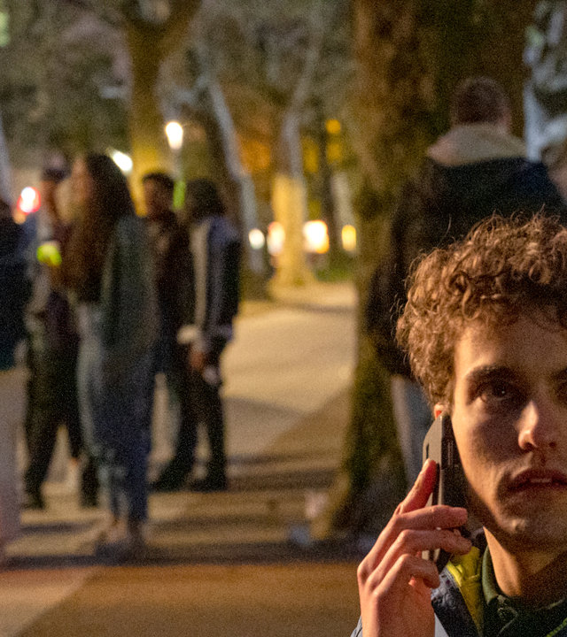 "SOKO Stuttgart - Partyzone": Marvin Kampfer (Lasse Möbus) sitzt bei Nacht auf einer Parkbank und hält sich mit der einen Hand sein Handy ans Ohr. In der anderen Hand hält er eine Bierflasche. Sein Blick ist erschrocken zur Seite gerichtet. Im Hintergrund stehen junge Menschen (Komparsen) mit Getränkeflaschen und unterhalten sich.