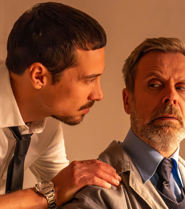 "SPYON - Die Lizenz zum Grillen": In einem Innenraum: Andreas (Klaus Steinbacher) steht hinter Hausmeister Harald (Matthias Matschke) und blickt zu ihm. Hausmeister Harald blickt seitlich über seine Schulter zu Andreas.