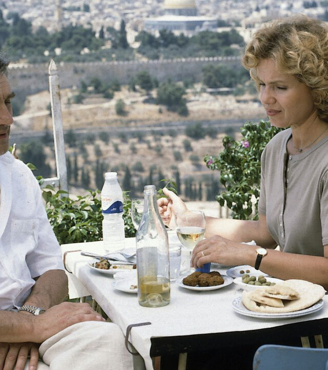 "Diese Drombuschs - Die Heimkehr“: Martin (Michael Degen) und Vera (Witta Pohl) sitzen auf einer Terrasse über den Dächer von Jerusalem an einem Tisch und essen gemeinsam.