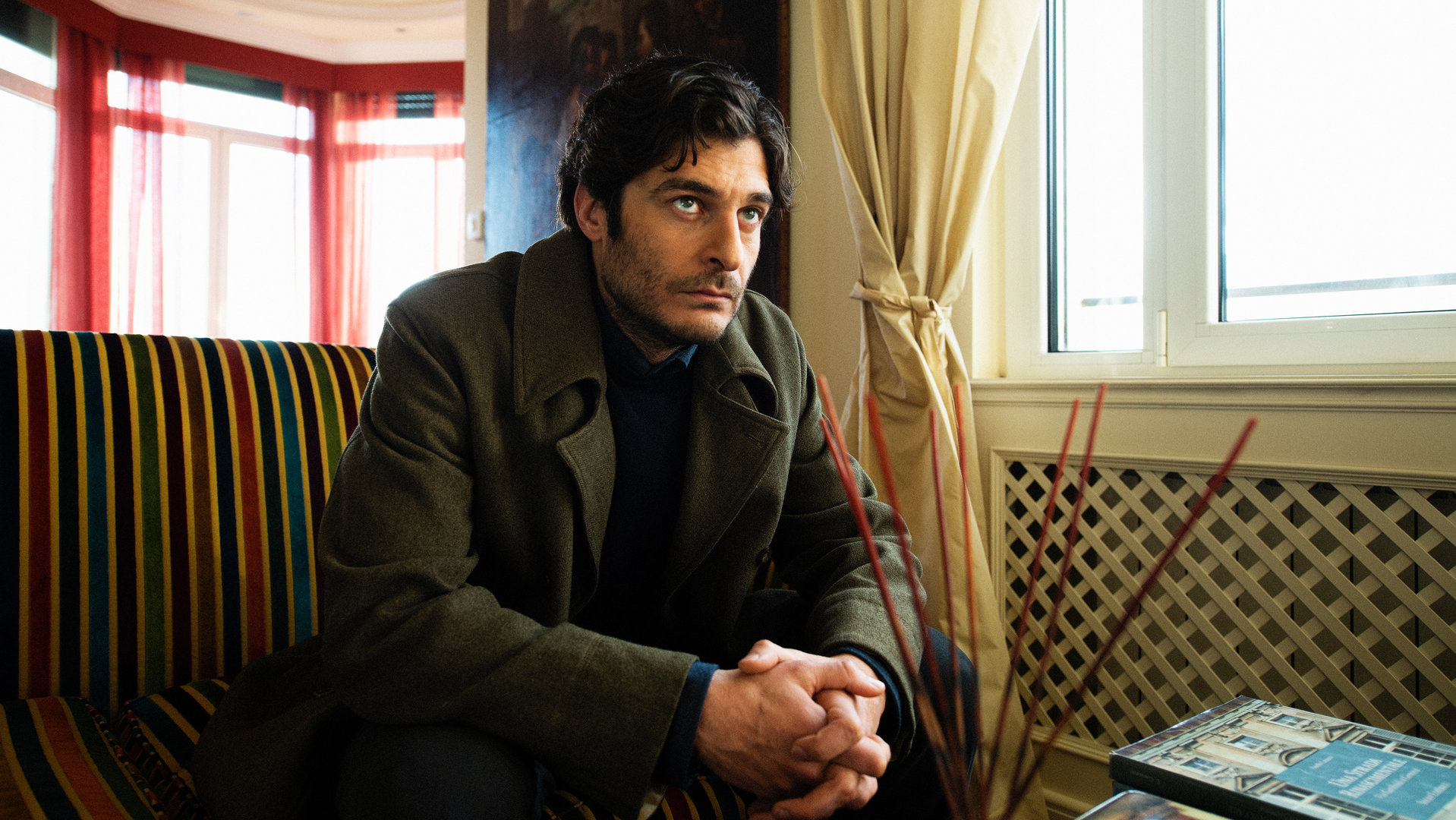 "Survivors - Freundschaften": Luca (Lino Guanciale) sitzt in seinem Wohnzimmer auf der Couch und blickt sorgenvoll nach vorne.
