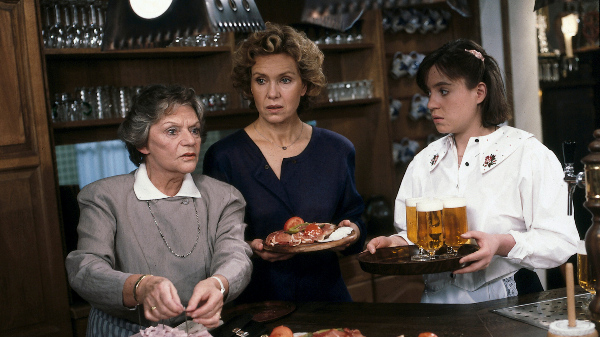 "Diese Drombuschs - Späte Einsicht": Oma (Grete Wurm), Vera (Witta Pohl) und Yvonnche (Anja Jaenicke) stehen nebeneinander hinter dem Tresen und unterhalten sich.