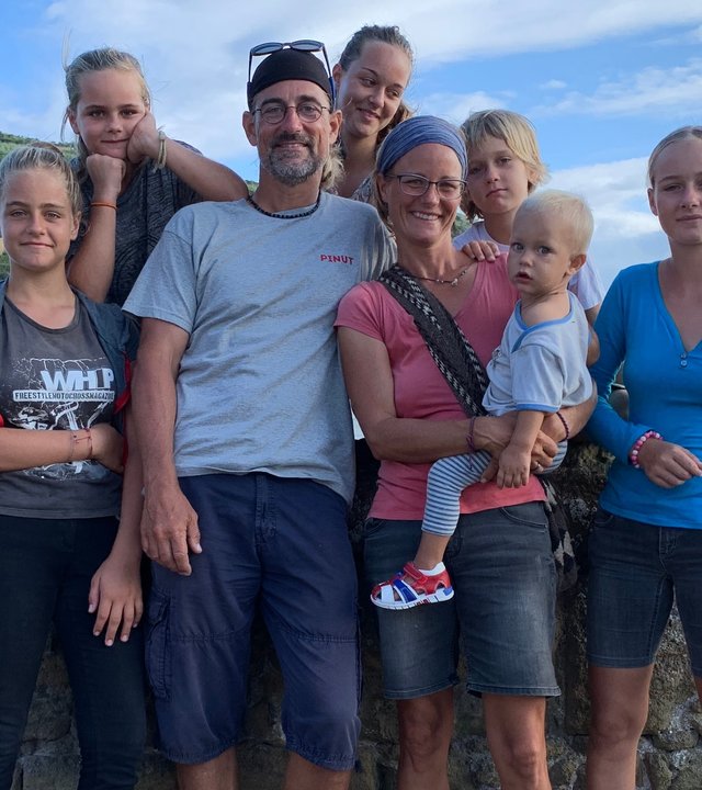 "37°: Aus und ahoi – Eine Großfamilie streicht die Segel": Die Großfamilie, Vater, Mutter und die sechs Kinder in von Kleinkind bis zum Jugendlichen stehen an einer Kaimauer. Im Hintergrund ist eine Meeresbucht und ein eine grüne Hügellandschaft zusehen.