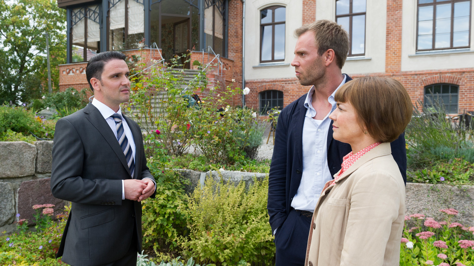 "SOKO Wismar - Femme fatale": Wolf Baumgart (Sascha Göpel), Lars Pöhlmann (Dominic Boeer) und Katrin Börensen (Claudia Schmutzler) stehen sich in einem Garten gegenüber und unterhalten sich.